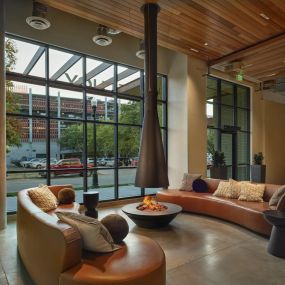Midcentury modern resident lounge space with an indoor fire pit and chic black flame hood extending from the ceiling with large metal grid-style windows and two brown leather-style couches