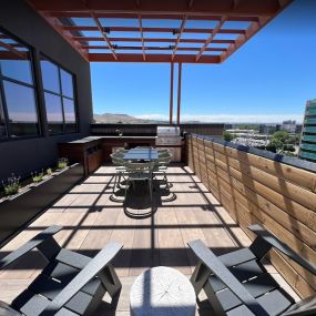 Chic rooftop lounge area with two black lounge chairs and bleached-wood stump-style side table in between with a view of the resident barbeque area and the Boise foothills