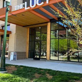 The Lucy entrance with an orange metal awning, white property name, and manicured landscaping