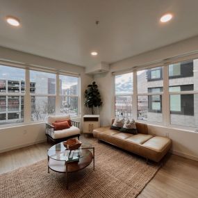 Spacious living area with a brown leather-style couch, jute-knotted rug, and two sets over oversized windows that overlook downtown Boise