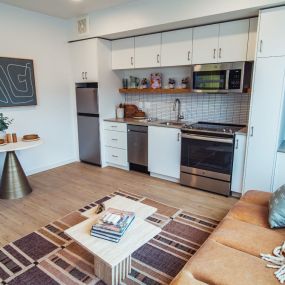 Kitchen and living room view with plank flooring, bistro-style dining area with a green accent chair, and modern abstract art above