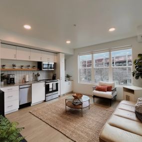 An open-style living room with view into the  kitchen, cozy seating area with a coffee table, and large windows