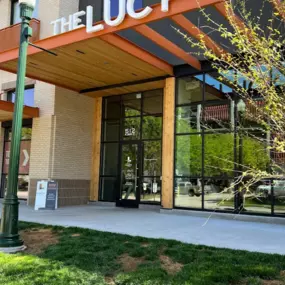 The Lucy entrance with an orange metal awning, white property name, and manicured landscaping