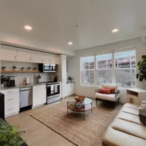 An open-style living room with view into the  kitchen, cozy seating area with a coffee table, and large windows