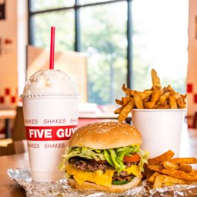 A Five Guys cheeseburger, milkshake and regular order of fries sits on a table inside a Five Guys restaurant.
