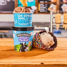 Waffle cone, cup and fresh packed pint in front of Ben & Jerry's ice cream shop menu board.