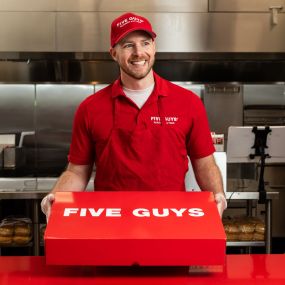 A Five Guys employee holds the red Five Guys catering box at the counter.