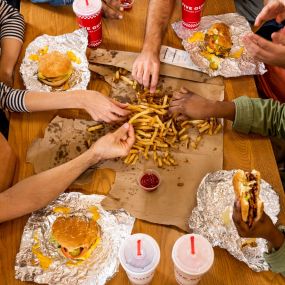 A top-down photograph of a group of friends sharing an order of fries alongside their sandwiches at a Five Guys restaurant.
