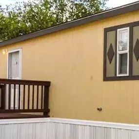 a yellow house with a wooden deck and a tree in the background