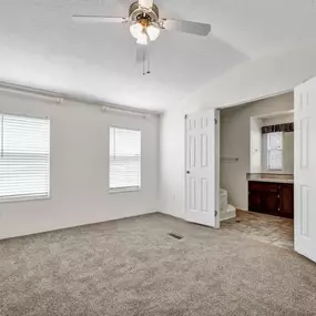 a bedroom with a ceiling fan and a bathroom in the background