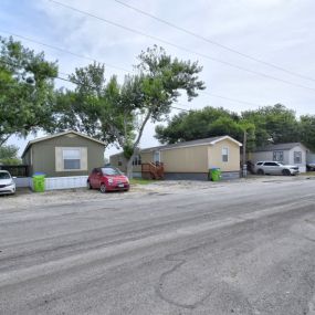 a gravel road in front of a row of houses with trees in the background