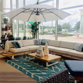 Elegant beige outdoor sectional with a wooden coffee table, stylish accents, and a large umbrella.