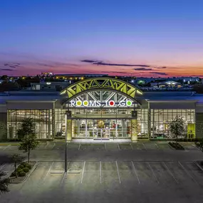 Dusk view of Rooms To Go store entrance with vibrant lighting.