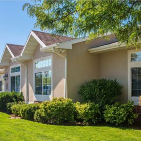 Side view of Oakstone Apartments leasing office with manicured green lawn and shrubbery lining the walls, while large, oversized windows look out into the grass