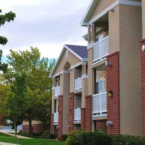 View of Country Oaks apartment building 4 with red brick, white beam balconies, and manicured grass pathways with trees