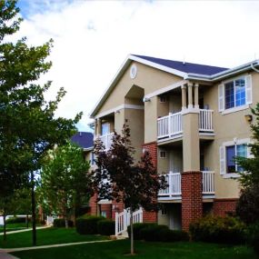 Country Oaks Apartment building with half-wall red brick work, white balconies, and tree lined pathways on a sunny day with a blue sky and white clouds