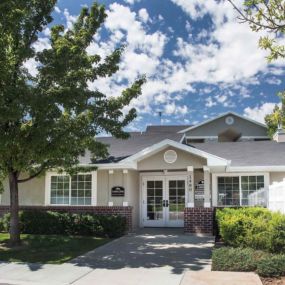 Front view of Country Oaks Apartments leasing office with double French doors, paned with glass, a white fence to the left, manicured grassy area on the right, and a brick half wall ending below the windows