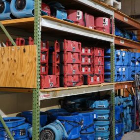 Interior view of PeachState Restoration warehouse with metal shelves holding organized red and blue restoration equipment like dehumidifiers and fans.