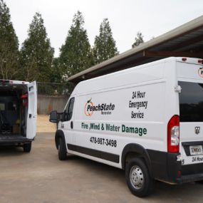 PeachState Restoration service vans parked behind a building, one with rear doors open showing interior shelving and equipment.