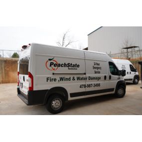 Side view of a PeachState Restoration service van with advertising for restoration services and contact information, another van in the background.