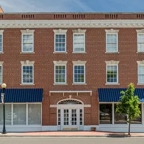 three-story building with a red brick facade, a central arched entrance with white double doors, and two large storefront windows with blue awnings.