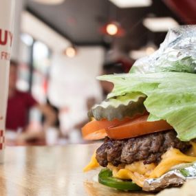 A close-up photograph of a Five Guys cheeseburger with pickles, tomatoes and jalapenos in a lettuce wrap.