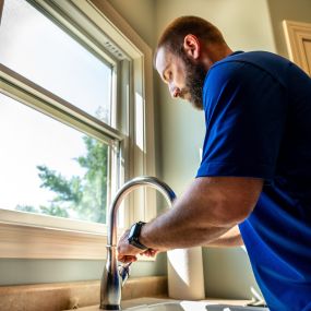 A Covenant Plumbing plumber stands confidently above a sink, ready to tackle any plumbing issue. The plumber is in uniform, showcasing their professionalism and expertise in Bloomington-Normal, IL