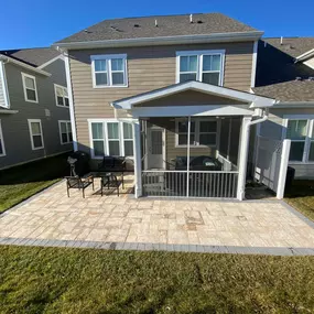 A professional hardscaping project underway in a Delaware home's backyard. The image shows landscapers laying irregular stone pavers to create a winding pathway. The scene includes a variety of landscaping tools and materials like sand and stone, with a partially completed patio area visible in the background. The house and garden display early spring foliage.