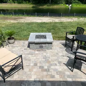 A cozy backyard in Delaware featuring a circular stone firepit surrounded by a ring of rustic wooden chairs. The firepit is lit, casting a warm glow on the faces of several people enjoying the evening. Lush greenery and trees can be seen in the softly lit background, enhancing the intimate outdoor setting.