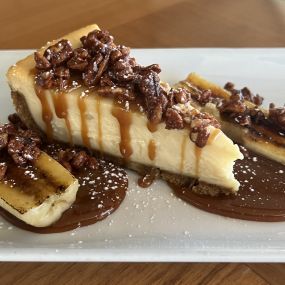 Banana Fosters Cheesecake dessert featuring cheesecake, candied pecans, Banana rum caramel and whipped cream.