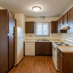 a kitchen with wooden cabinets and white appliances with a small widow above the sink.