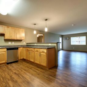 an empty kitchen and living room with wood floors and wood cabinets.