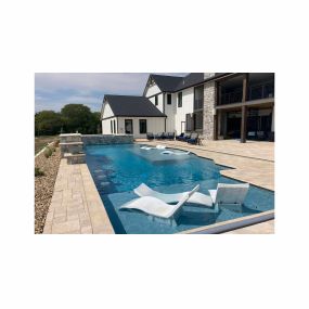 Pool in a backyard with two in-water tanning decks with beach chairs on them