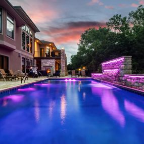 Backyard pool with waterfall and lights making the pool and waterfall appear purple