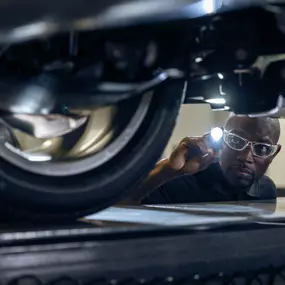 A service technician looking under a vehicle with a flashlight