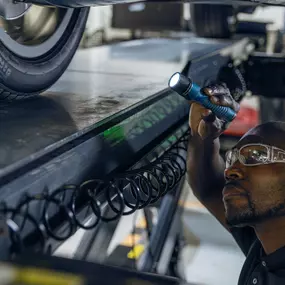 A service technician looking under a vehicle with a flashlight