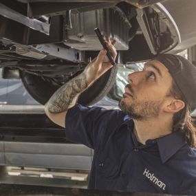 A service technician looking under a vehicle with a flashlight