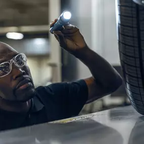 A service technician looking under a vehicle with a flashlight