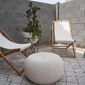 a patio with two chairs and a white ottoman and a mirror and plants