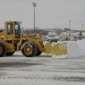 Small machine plowing snow in a parking lot.