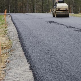 Smooth Paving asphalt pavement machine in the background, close up view of a fresh asphalt overlay.