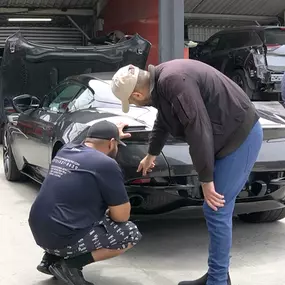 Detailing team inspecting Aston Martin at auto body shop parking lot after a successful collision repair