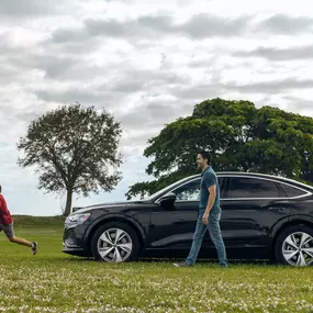 New Audi parked on the grass in front of trees with people running