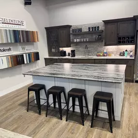 This image showcases a kitchen display in the Focal Point Flooring showroom. The centerpiece is a large kitchen island with a stunning granite countertop. The island is surrounded by stylish bar stools.