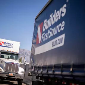 Builders FirstSource semi-trucks on a lot with clear mountain views in the background, showcasing reliable transportation and expansive reach across regions.