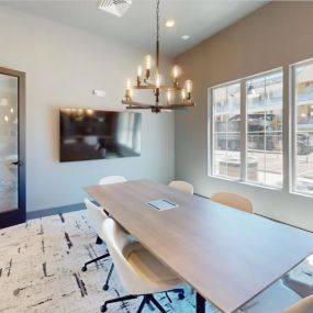 a conference room with a long wooden table, chic chandelier, and chairs surrounding with a TV and large, oversized windows