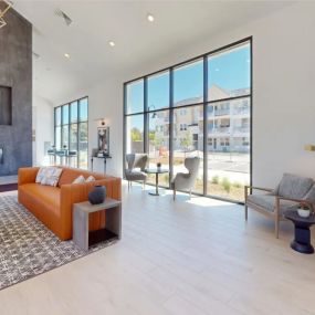 The open, spacious resident lounge with an orange couch, coffee table, and large windows