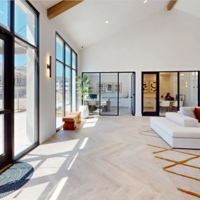 The oversized resident lounge with a cream couch, herringbone pattern plank flooring, oversized windows, and a large glass door