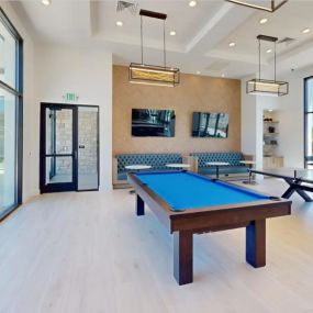 a game room with a pool and ping pong tables with booth seating and large windows