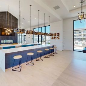 The large resident entertainment, game, and demo kitchen area with bar seating and pendant lighting, with a pool table and oversized windows